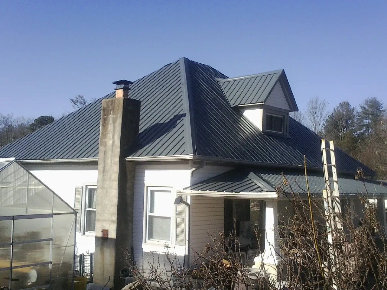 Dark blue standing seam metal roof on a white farmhouse with dormer — Slate & Tile Roof Repair by Roofing Brothers in Clarks Hill