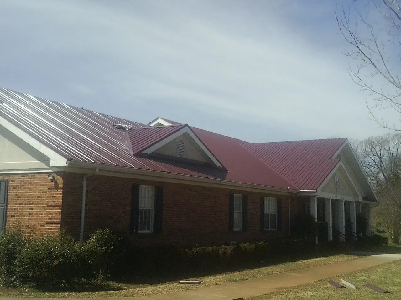Red metal roof with gabled entries on a long brick building, from a Hail Damage Roof Repair job in Clarks Hill